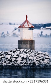 Small iced out lighthouse on snowy rocks near ice cold lake