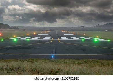 Small illuminated runway of a country airport. Dark dramatic cloudy sky. Aviation industry. Nobody. Selective focus. Dangerous flying conditions