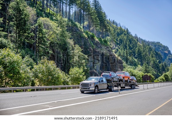 Small\
Industrial standard car hauler rig semi truck transporting cars on\
the modular one level semi trailer driving on the highway road\
along the Columbia River in Columbia Gorge\
area