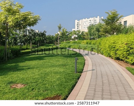 Small Interlock Path Between Landscaping Area.
Green And Lush Landscaping Area With Carpet Grass And Trees Like Palm Or Washingtonia, Some Houses Or Villa's Also Beside Gardens Padestrian Pathway.