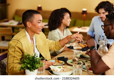 A Small Interracial Group Of Friends Is Sitting In A Restaurant And Having Dinner.