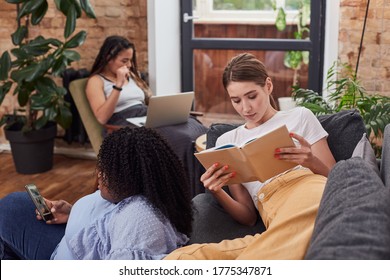 Small Interracial Group Of Three Young Ladies Roommates Communicating Online Or Reading While Being At Home