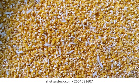Small, irregular yellow kernels, most likely corn or cracked corn. There are also a few scattered, lighter, elongated kernels mixed throughout.