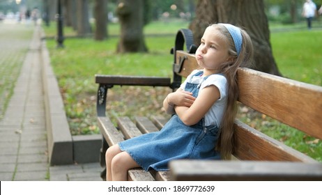 Kleines irritiertes Mädchen, das allein auf einer Bank im Sommerpark sitzt.