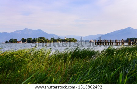 Small island “Frauenchiemsee“ with church and monastery is a tourist attraction on the Chiemsee alpine Lake in Bavaria Germany. Reed, ferry, sailboat and peer with mountain panorama in the background.