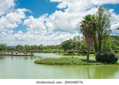 Small Island Inside A Lake With Green Trees In The Background And A Blue Sky With Clouds, No People