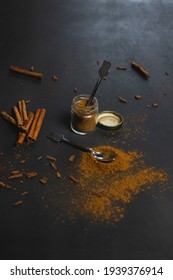 Small Jar Full Of Ground Cinnamon With A Tiny Spoon Inside And Cinnamon Sticks On The Side. On Black Background. Ceylon Cinnamon, Healthy Spice.