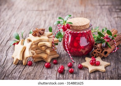 A small jar of homemade fresh spicy sweet cranberry sauce with cinnamon next to a stack of homemade gingerbread cookies in the shape of stars on a dark wooden background. selective Focus