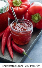 A Small Jar Of Homemade Red Hot Pepper Jelly Surrounded By Red Peppers