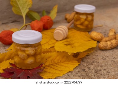 Small Jar With Honey And Nuts On Yellow Leaves. Selective Focus. The Concept Of Homemade Healthy And Environmentally Friendly Food. In The Background Is A Wooden Honey Spoon.