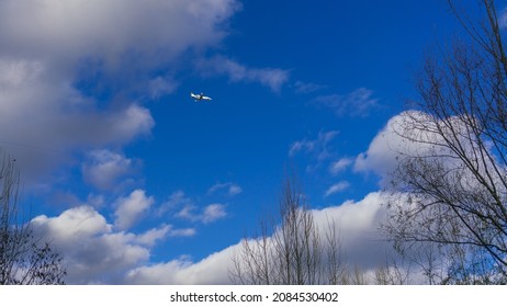 Small Jet Plane In The Cloudy Sky Over Autumn Trees With Fallen Leaves On A Sunny Day