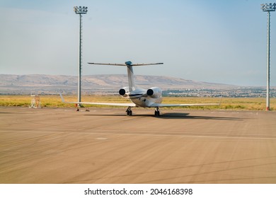 A Small Jet Plane Stands On The Runway Against The Background Of Distant Mountains And Blue Sky. Transport And Travel For Business And Tourism. Copy Space