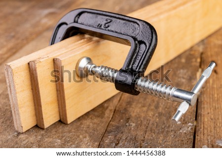 A small joinery clamp used for gluing planks. Accessories for carpenters on the workshop table. Dark background.