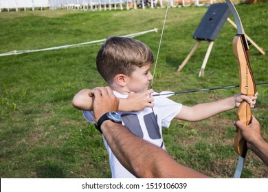 Small Kid With Bow And Arrow Learning To Aim At The Target With Help Of Archery Instructor. 