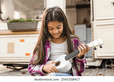 Small kid child daughter preteen girl playing ukulele guitar while traveling driving by camper van trailer, caravanning by motor wheel home. Away from everything, adventures ahead - Powered by Shutterstock