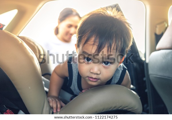 small kid climbing and\
crawling to child car seat inside suv car with mother standing in\
background blur