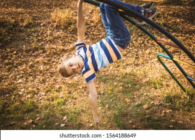 Small Kid Handing On Monkey Bars While Playing Outdoors At The Playground. 