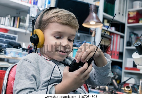 Small kid with\
head phones talking over CB radio in amateur radio station. Little\
boy using walkie talkie.