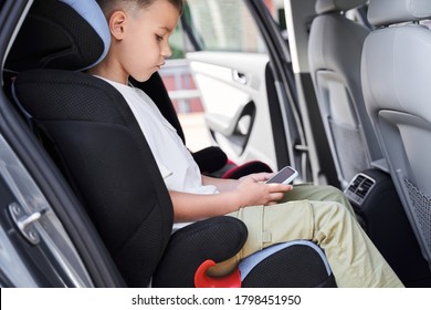 Small Kid Is Sitting In Child Seat And Using Smart Phone For Pleasure While Travelling