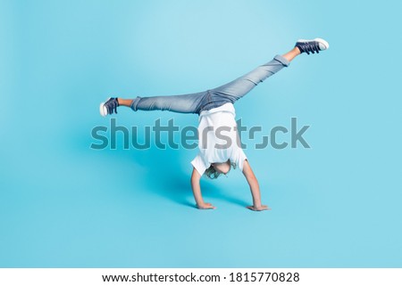 Small kid stand hands do acrobatic trick wear white shirt jeans sneakers isolated blue color background