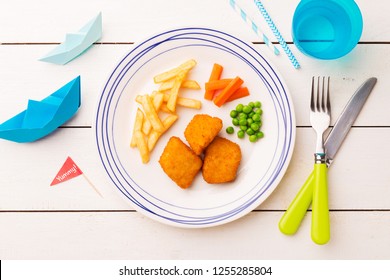 Small Kid's Meal - Fish, Chips, Carrot And Green Peas. Colorful Dinner On White Wooden Table. Plate Captured From Above (top View, Flat Lay). 