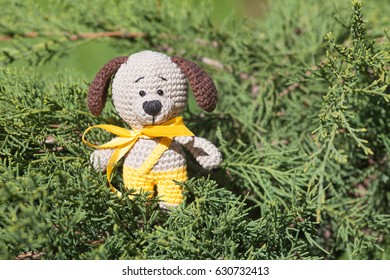 A small knitted brown dog with a yellow ribbon in summer garden. Knitted toy, handmade, amigurumi