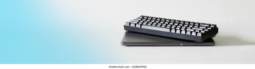Small laptop   trendy black mechanical computer keyboard for esports white   blue gradient background  Wireless keyboard for laptop  Side view  Copy space  Web banner  Close  up