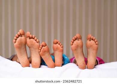 Small and large bare feet, three pairs of barefoot close-up, children lying on the bed. Foot Relaxing. Family bonding generations concept. Childhood moments. - Shutterstock ID 2362482721