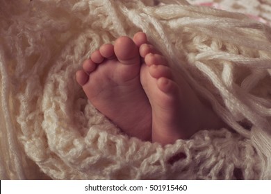 Small legs baby bundled up in a white knitted blanket