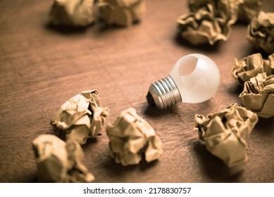 A Small Light Bulb With A Broken Hole Among The Crushed Paper Balls, Mistake, Lost Idea And Solution, Problem Idea Needs Improvement, Or Fail Concept