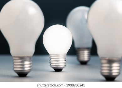 Small Light Bulb Is Glowing In The Group Of The Big Light Bulbs, Small Business In Competition Idea, Or Coaching And Success Training Concept