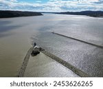 small lighthouse on the hudson river with stone line sea wall in water (rondout creek with clouds hills daytime drone shot photo from above) photography landscape beacon for ships boats kingston ny