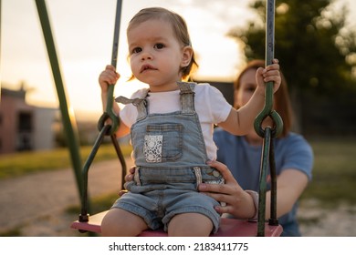 Small Little Girl Toddler With Her Mother In Park Woman Help Her Child To Swing While Having Fun Outdoor In Sunny Day Leisure Family Growing Up Concept Copy Space Real People