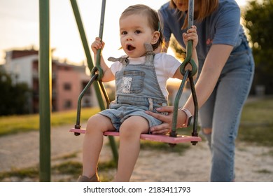 Small Little Girl Toddler With Her Mother In Park Woman Help Her Child To Swing While Having Fun Outdoor In Sunny Day Leisure Family Growing Up Concept Copy Space Real People