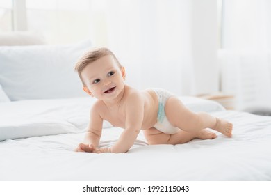 Small little smiling european infant toddler baby boy girl son daughter in diaper crawling on the comfy bed with white linen, first steps, motherhood,dryness and absorbency concept