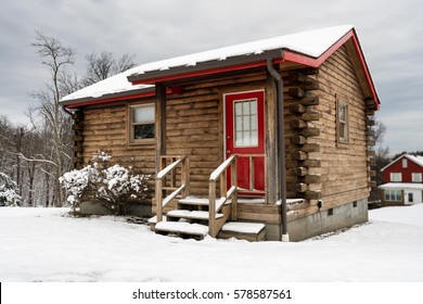 Small Log Cabin On Snowy Winter Day With Steps Leading Up To Red Painted Door.