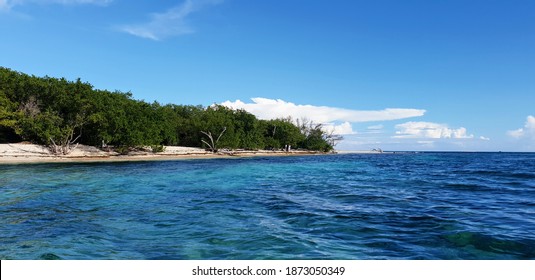 Small luscious green island with white sand beach sitting in crystal-clear glistening blue Jamaican waters in the Port Royal Habour of Kingston Jamaica 