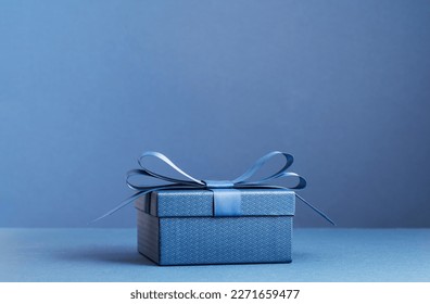 small Luxury gift box with a blue bow on dark blue. Side view monochrome . Fathers day or Valentines day gift for him. Corporate gift concept or birthday party. Festive sale copy space - Powered by Shutterstock