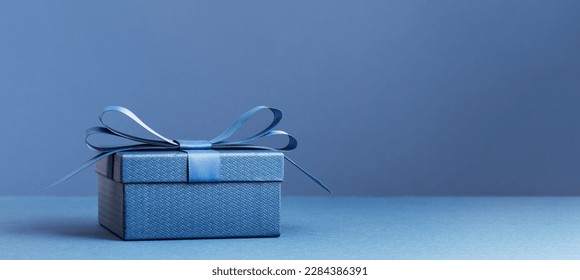 small Luxury gift box with a blue bow on dark blue table. Side view monochrome . Fathers day or Valentines day gift for him. Corporate gift concept or birthday party. Festive sale copy space banner - Powered by Shutterstock
