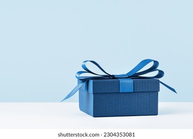 small Luxury gift box with a blue bow on light blue. Side view monochrome . Fathers day or Valentines day gift for him. Corporate gift concept or birthday party. Festive sale copy space