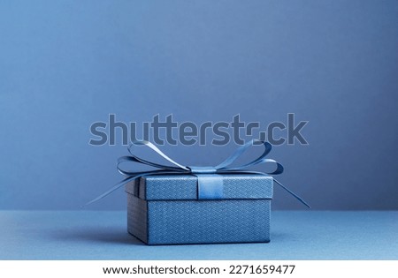 small Luxury gift box with a blue bow on dark blue. Side view monochrome . Fathers day or Valentines day gift for him. Corporate gift concept or birthday party. Festive sale copy space