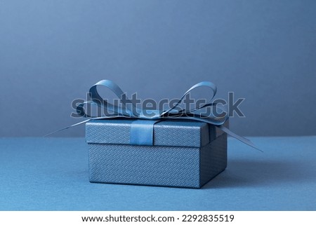 small Luxury gift box with a blue bow on dark blue. Side view monochrome . Fathers day or Valentines day gift for him. Corporate gift concept or birthday party. Festive sale copy space
