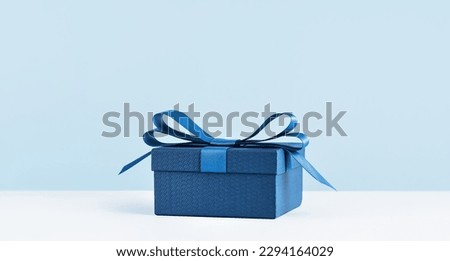 small Luxury gift box with a blue bow on light blue. Side view monochrome . Fathers day or Valentines day gift for him. Corporate gift concept or birthday party. Festive sale copy space