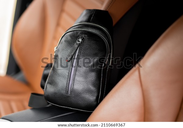A small men\'s leather\
backpack in the cabin of a luxury car. Black men\'s leather car seat\
bag.