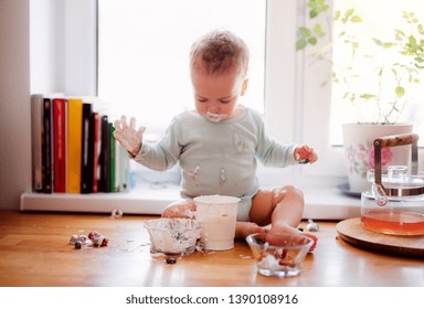 A Small Messy Toddler Boy Sitting On Kitchen Counter At Home, Eating.