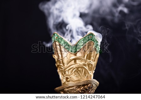 Small metal decorative Arabian Bakhoor incense burner censer with smoke and black background.

