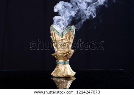 Small metal decorative Arabian Bakhoor incense burner censer with smoke and black background.
