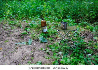 A small metal table with a cup and a bottle of beer on it. The table is surrounded by green grass and leaves - Powered by Shutterstock