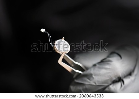 Small microphone of the overhearing device, spy holding a microphone with tweezers, black gloves. Micro listening device, soft focus