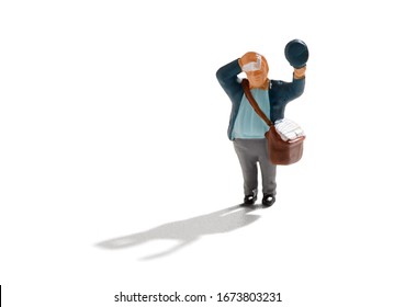 Small miniature figure of a sweaty hot postman lifting his cap to wipe his brow with a handkerchief with his satchel of letters on his shoulder over white with shadow - Shutterstock ID 1673803231